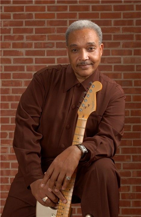 Johnny Rawls portrait by brick wall with guitar